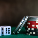 Two dice and a stack of colorful casino chips on a green surface